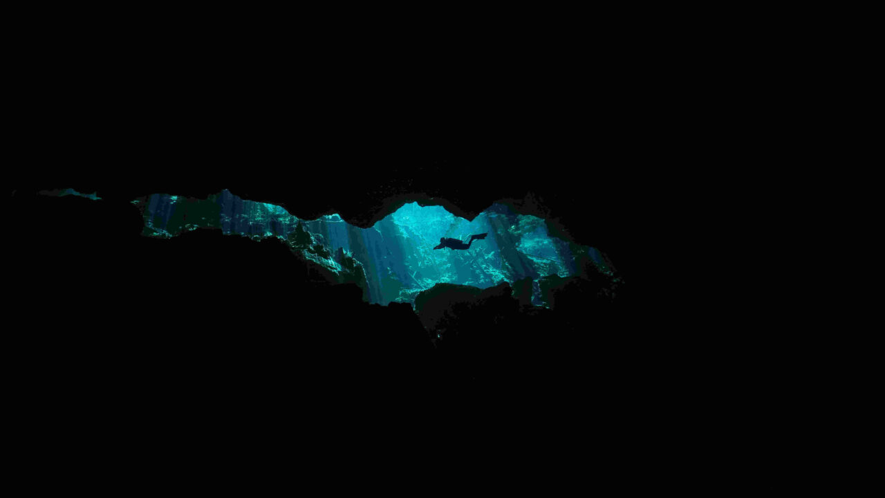 Silhouette d’un plongeur devant une ouverture éclairée dans une cavité immergée.